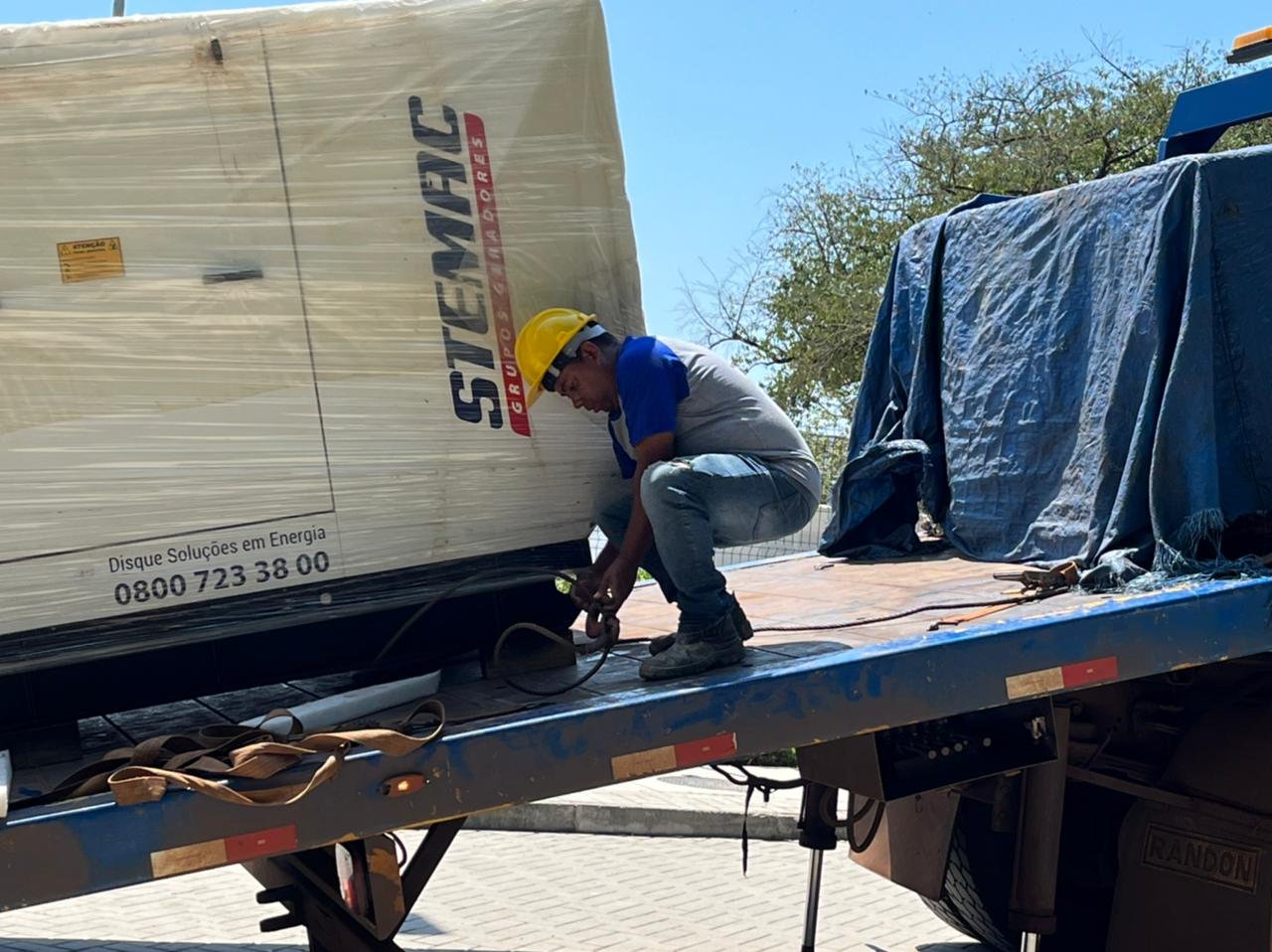 Profissional com capacete ao lado de um grupo gerador sobre um caminhão